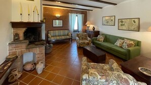 Ein gemütliches Wohnzimmer mit Kamin, einem grünen Sofa, einem gemusterten Sessel und einem Fliesenboden.