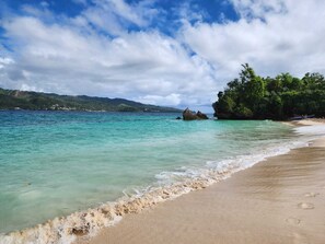 A beach with clear turquoise water, a sandy shore, and a backdrop of green hills. - Best Amazing Direct Ocean Beach Pool Views from Penthouse - Winter Specials (Las Terrenas)