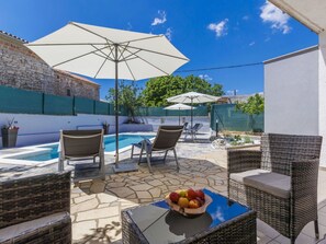 Relax by the pool surrounded by lush greenery and a stone building.