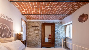 A bedroom with a brick ceiling, stone walls, a large bed, a wooden door, and a window with curtains. - Lovely apartment for 2 people with WIFI, pool and TV (Monastero Bormida)