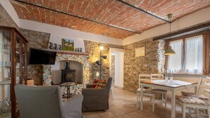 A cozy living room with a tiled floor, a fireplace, a television, and a dining area with a table and chairs. - Lovely apartment for 2 people with WIFI, pool and TV (Monastero Bormida)