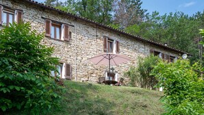 A stone building with a tiled roof, wooden shutters, and a small patio area with a table and chairs. - Lovely apartment for 2 people with WIFI, pool and TV (Monastero Bormida)