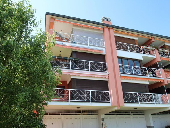 Un immeuble résidentiel à plusieurs étages, doté de balcons, d’un garage et d’un arbre au premier plan.