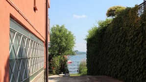 Eine terrasse mit Steinplatten und Blick auf einen See, mit einem roten Gebäude und einem Fenster mit geometrischem Muster.