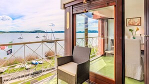 Ein Balkon mit einem Korbstuhl, einer Glastür, die zu einem Zimmer führt, und Blick auf Boote auf einem See.