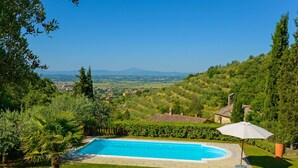 Une piscine entourée d’une végétation luxuriante, avec vue sur des collines lointaines et un petit bâtiment en arrière-plan.