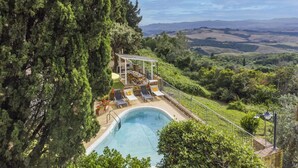 Un espace piscine agrémenté d’une pergola, de chaises longues et offrant une vue sur des collines verdoyantes.