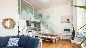 Un salon moderne avec un canapé bleu foncé, une table à manger en bois et un escalier menant à un niveau supérieur.