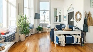 Un salon spacieux doté d’un plancher en bois, d’un canapé blanc, d’un canapé bleu, d’une table basse et d’une grande fenêtre laissant entrer la lumière naturelle.