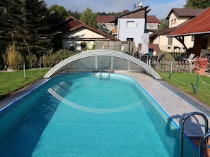 A swimming pool with a curved glass enclosure, surrounded by a wooden fence and a grassy area. - Beautiful apartment for 4 guests with pool, WIFI, TV and patio (Jablonec Nad Nisou)