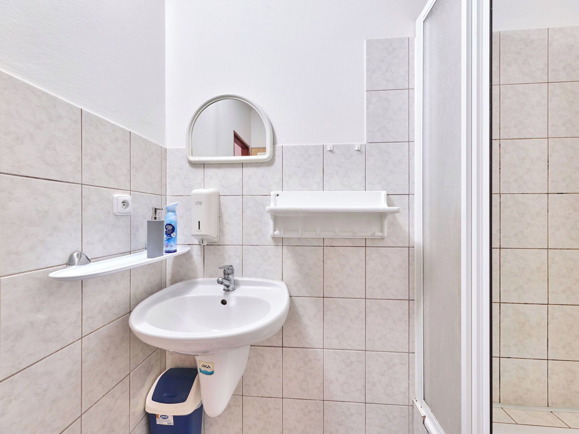 A bathroom with a white sink, a mirror, a soap dispenser, and a towel dispenser.