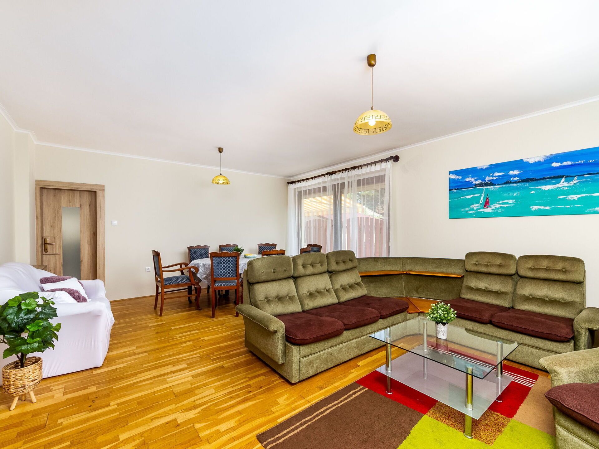 A living room with a sectional sofa, a glass coffee table, and a dining area with a table and chairs.