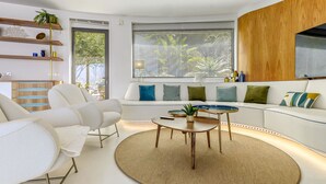 A modern living room with a white sofa, a round coffee table, and a large window with blinds. - Beautiful private villa for 8 guests with WIFI, private pool, A/C, TV and terrace (Roses)