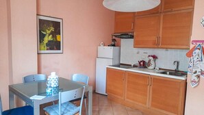 A compact kitchen with wooden cabinets, a white refrigerator, and a dining table with chairs.