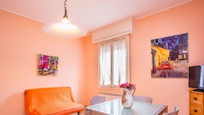 A dining area with a glass table, chairs, a sofa, a vase with flowers, and a painting on the wall.