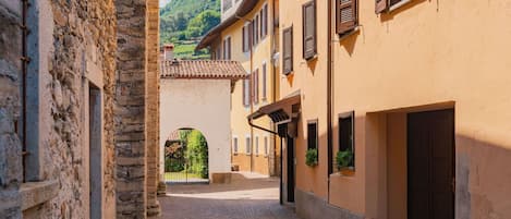 A narrow cobblestone street flanked by historic buildings with arched doorways and shuttered windows.