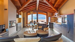 Ein modernes Wohnzimmer mit hohen Decken und Holzbalken, ein Essbereich mit Blick und eine Küche mit Edelstahlgeräten.
