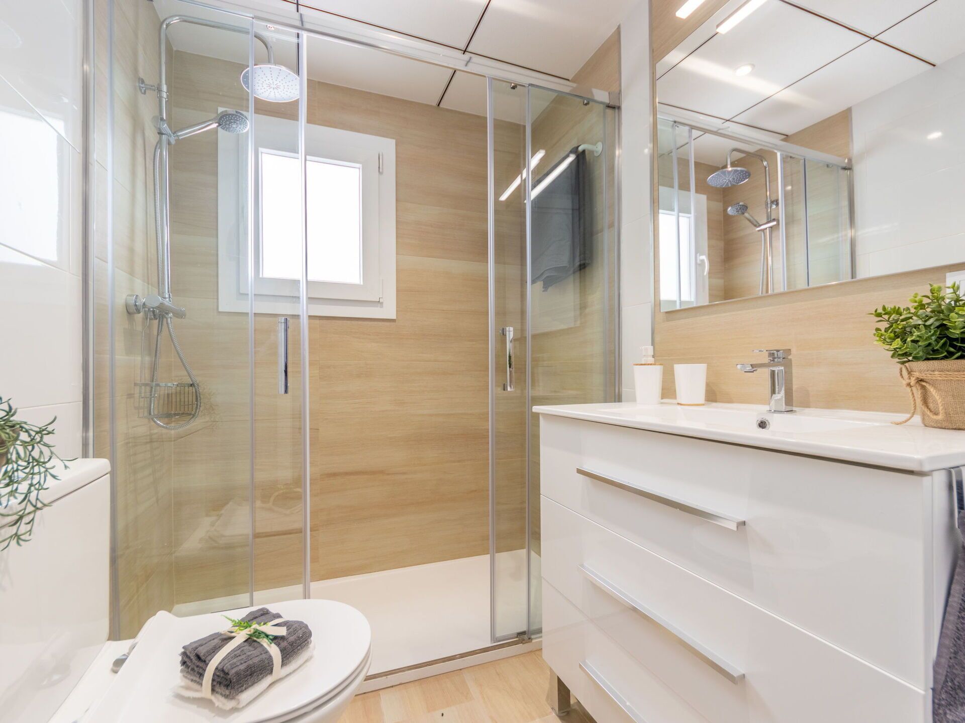 Une salle de bain moderne avec une douche à parois de verre, un meuble-lavabo blanc doté d’un miroir et une petite plante en pot.