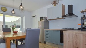A modern kitchen with wooden flooring, a dining area with a table and chairs, and a view through a large window.