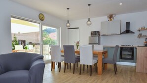 A modern kitchen with a dining area, featuring a large window, a clock, and a built-in oven.