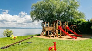 A playground with a slide and swings, set against a lake and trees.
