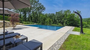 A swimming pool with a stone border, surrounded by a grassy area and trees. There are lounge chairs and a table with a hat and bottle. - Wonderful  villa for 6 people with private pool, A/C, WIFI, TV and terrace (Pazin)