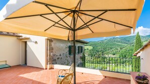 A balcony with a large umbrella, wicker chairs, and a potted plant.