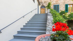 A staircase leading to a stone building with a wooden door and green shutters.