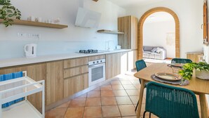 A modern kitchen with a central island, wooden cabinets, and a dining area with wicker chairs and a table. - Wonderful private villa for 3 people with WIFI, A/C, TV, patio and pets allowed (Guardistallo)
