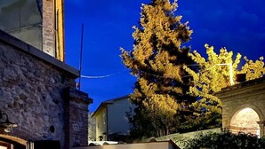 An outdoor patio area with two wicker chairs and a small round table, a stone wall, and a large tree in the background. - Wonderful private villa for 3 people with WIFI, A/C, TV, patio and pets allowed (Guardistallo)