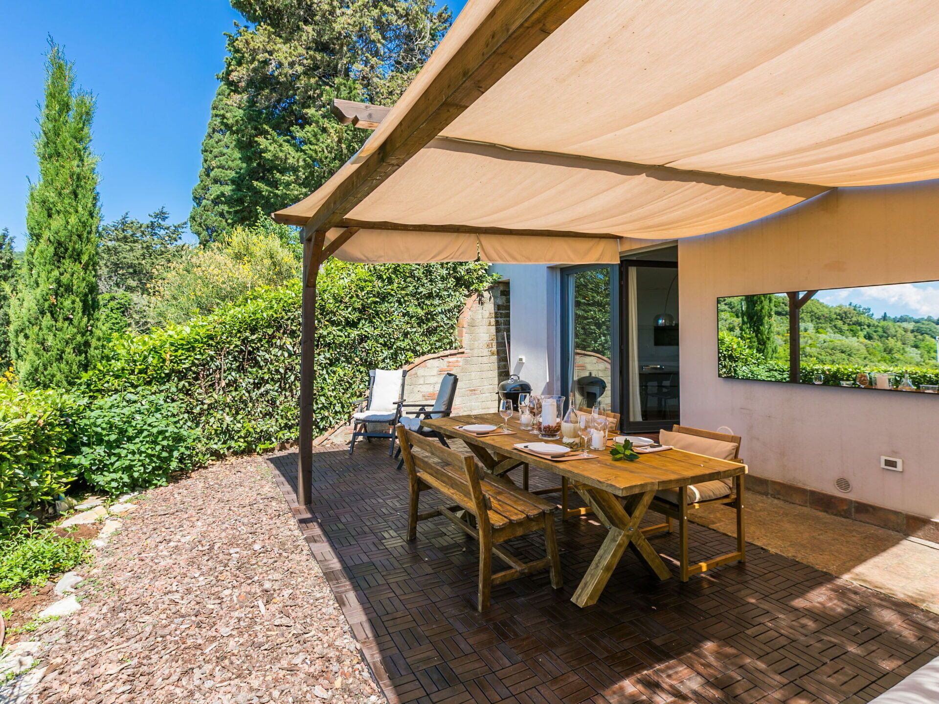 Un espace extérieur aménagé pour les repas, avec une table et des chaises en bois, une pergola offrant de l’ombre et une vue sur la verdure environnante.
