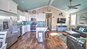 Cozinha ampla com eletrodomésticos modernos, sala de jantar com sofá de couro e sala de estar com televisão e objetos decorativos.