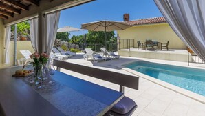 Ein Poolbereich mit Liegestühlen, einem Tisch mit Blumenvase und Blick auf Pool und Grünflächen.