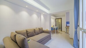 Una sala de estar moderna con un sofá, un comedor con sillas y una cocina visible a través de una puerta abierta.