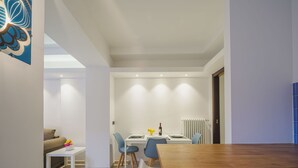 Un comedor moderno con una mesa de madera y sillas azules, un sofá blanco y una pequeña mesa blanca con un florero.