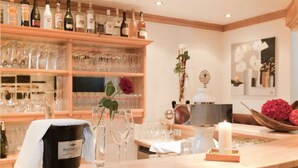 A bar area with a wooden counter, shelves with bottles and glasses, a bucket, and a vase with a rose.