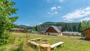Ländliche Szenerie mit einem Holthaus, Picknicktischen und freiem Blick auf einen bewaldeten Gebirgszug.
