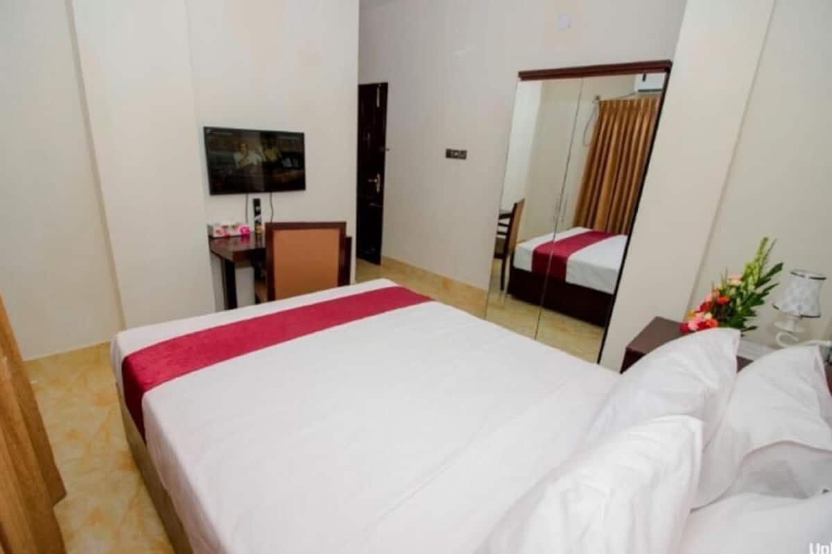 A hotel room with a bed, a desk, a chair, a television, and a mirror.
