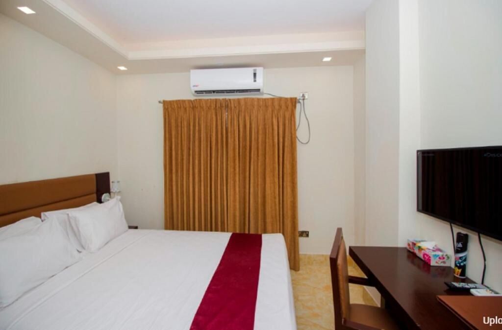 A hotel room with a bed, a TV, an air conditioning unit, and a curtain.
