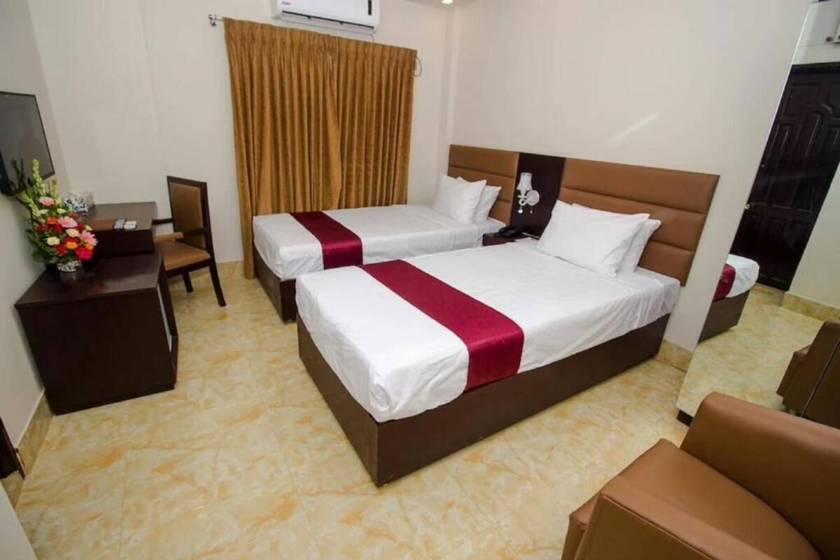 A hotel room with two beds, a desk, a chair, a TV, and a curtain.