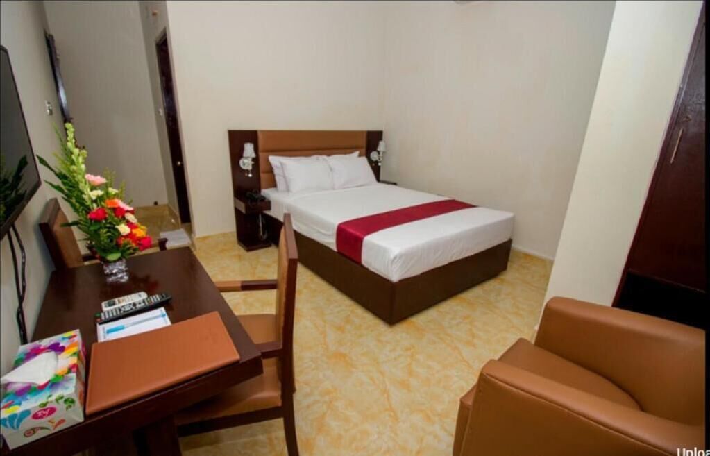 Een hotelkamer met een bed, een bureau met een bloevas, een stoel en een bruine bank.