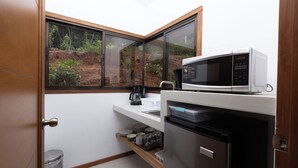 A compact kitchen with a microwave, refrigerator, and a window with a view of greenery. - Casa Kabuae (Savegre)