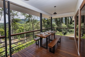 Une terrasse en bois avec une table et des bancs, offrant une vue sur une forêt luxuriante et des montagnes.