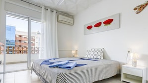 Een moderne slaapkamer met een groot bed, balkon uitzicht en een schilderij van rode bloemen aan de muur.