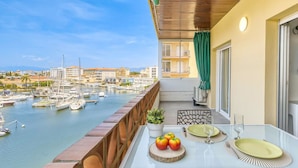 Een balkon met een tafel gedekt voor twee, met uitzicht op een jachthaven met boten en gebouwen.