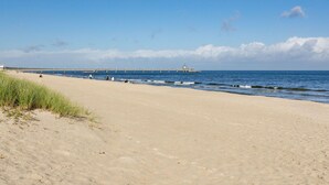 Une plage avec une jetée qui s’avance dans la mer, et à l’extrémité de laquelle se trouve une petite construction.