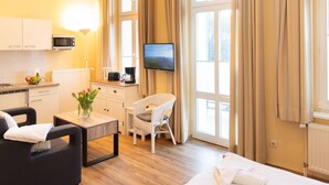 Une chambre d’hôtel comprenant un lit, un canapé, une table à manger, un téléviseur, un coin cuisine et de grandes fenêtres avec des rideaux.