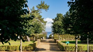 Un sentier pavé mène à un plan d’eau, bordé d’arbres et de haies.