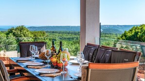 An outdoor dining area with a table set for two, featuring wine glasses, bottles, and a fruit bowl. - Awesome home in Trget (Trget)