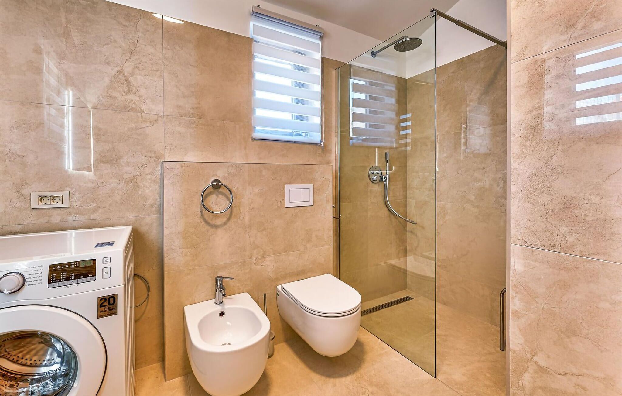 Une salle de bain moderne dotée d’une douche à parois de verre, d’un bidet, de toilettes et d’un lave-linge.